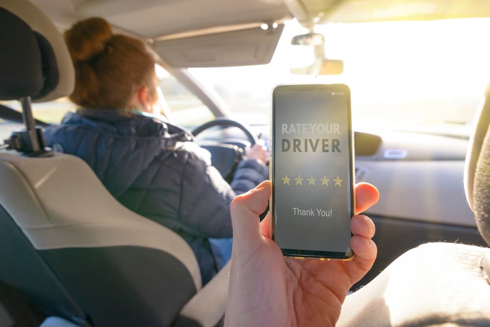 Passenger is sitting on the back seat of the car and using smart phone app to rate a rideshare driver