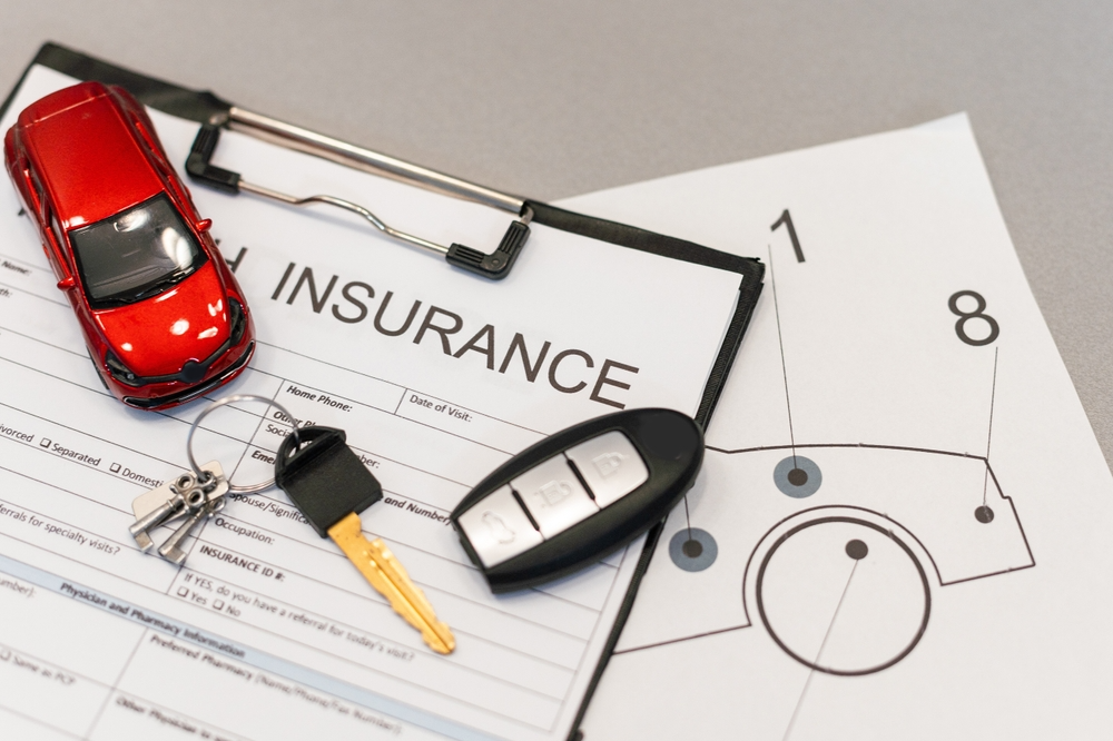 Person examining a car insurance policy document with a damaged car in the background, symbolizing protection after a car incident and reviewing coverage details.
