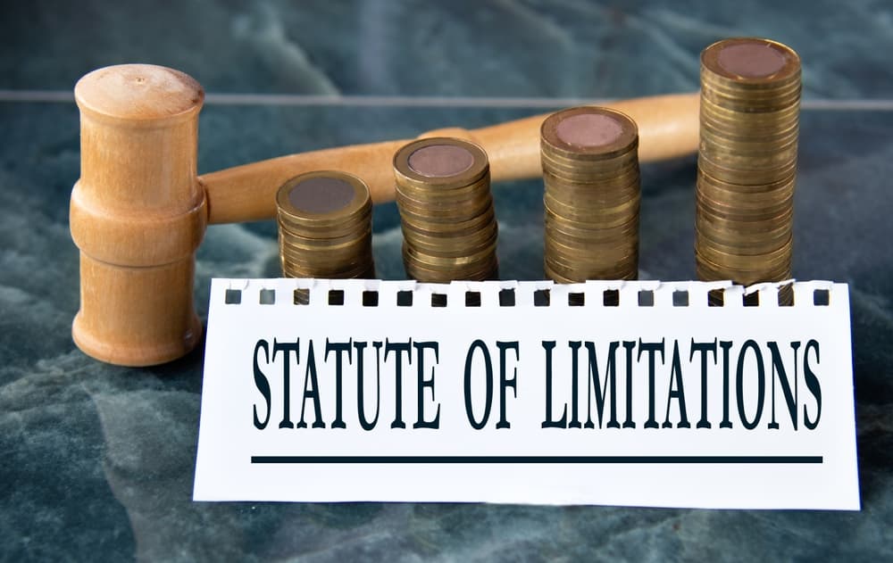 Statute of Limitations written on paper with judge's gavel and stack of coins in the background, symbolizing legal and financial consequences.